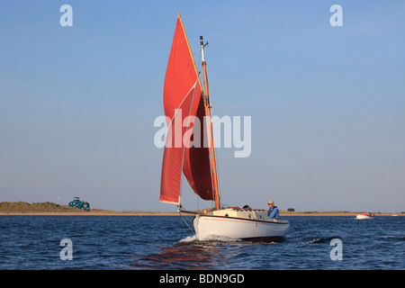 A yacht sailing in Blakeney harbour, North Norfolk, on a calm summer afternoon Stock Photo