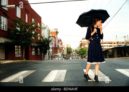 A young lady crossing the road on a zebra crossing holding an umbrella Stock Photo