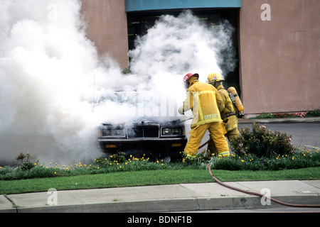 extinguish fire car auto smoke flame danger risk mask helmet oxygen tank hose spray put out fight Stock Photo