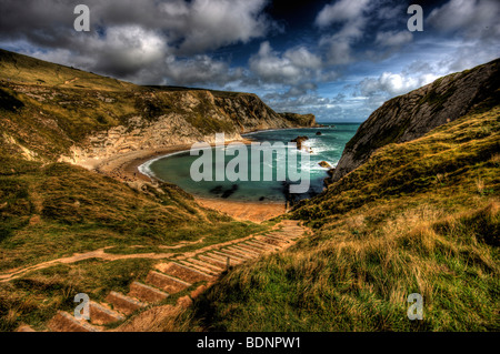 Uneven steps leading down in to Man of War bay in dorset looking out over a windy bay with white water breaking over rocks. Stock Photo