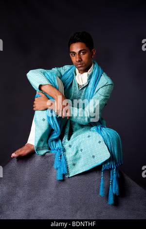 Beautiful authentic Indian hindu man in typical ethnic groom attire sitting relaxed on top of rock leaning on knee. Bangali male Stock Photo