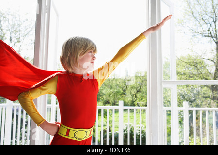 Portrait of young boy (7-9) wearing superhero costume, arm raised, indoors