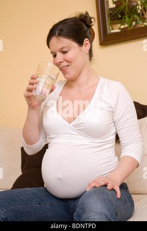 Pregnant woman sitting on a sofa drinking water Stock Photo