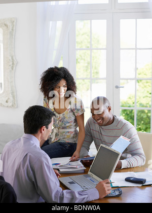 Young African American couple discussing home finances with financial advisor at dining room table Stock Photo