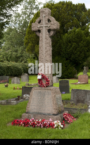 Cross shaped stone carved war memorial cenotaph in grassy graveyard / cemetery adorned with flowers and poppy wreath Stock Photo