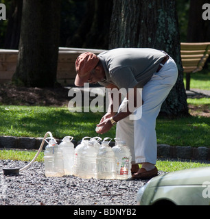 A man filling plastic jugs with fresh water with a hose. Stock Photo