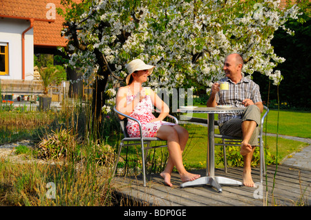 Couple drinking coffee at a garden pond in front of flowering cherry tree