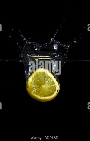 A lemon dropped into water creating a splash and bubbles. Isolated on black. Stock Photo