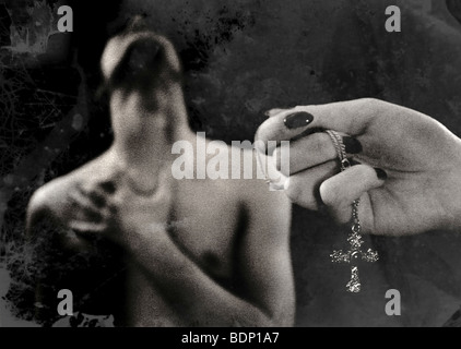 A young womans hand holding a silver cross with a male figure in the background Stock Photo