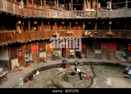 Chinese woman drawing water from the well in the courtyard of a wooden round house, Chinese: Tulou, adobe round house of the Ha Stock Photo