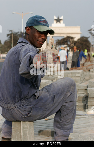 Road workers led by Chinese foreman repair the pavement near Independence Square and the Black Star monument arch. Stock Photo