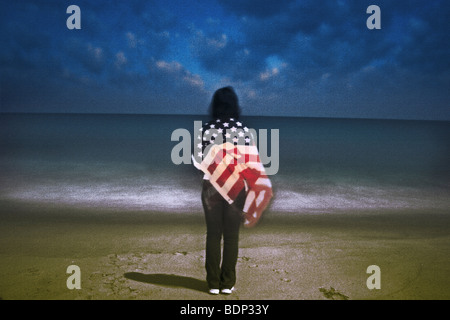 A figure holding a US flag standing on a beach Stock Photo