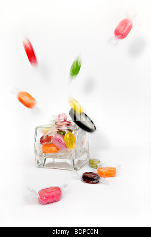Studio shot of coloured boiled fruity sweets exploding from glass jar against a white background with lid falling off Stock Photo