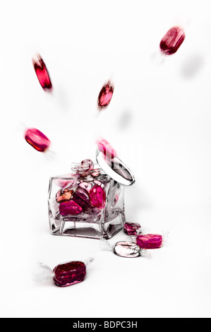 Studio shot of pink and red boiled fruity sweets exploding from glass jar against a white background with lid falling off Stock Photo