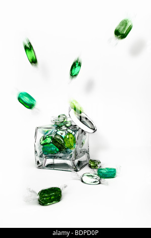 Studio shot of green boiled fruity sweets exploding from glass jar against a white background with lid falling off Stock Photo