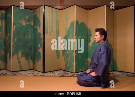 Young man in kimono sitting in front of folding screen Stock Photo