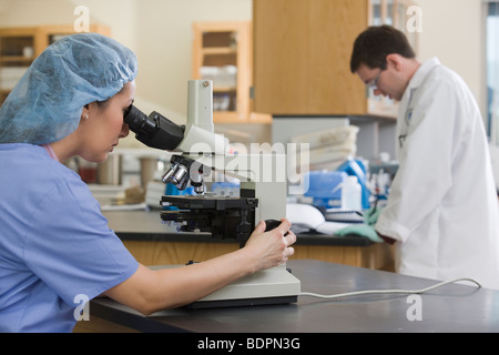 Female lab technician analyzing a sample through a microscope Stock Photo