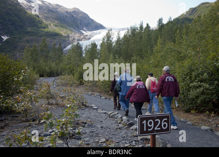 Visitors walk past a sign below Exit Glacier in Kenai Fjords National Park showing how far the glacier extended in 1926 Stock Photo