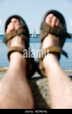 Feet with sandals and a sailing-boat Sweden. Stock Photo