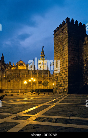 Giralda Tower and Cathedral on left at twilight with walls of the Alcazar on right, Seville, Spain Stock Photo