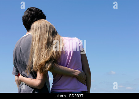 Romantic teenage couple looking at blue sky hugging. Back view. Stock Photo