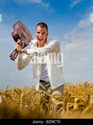 young man breaking a guitar in a rye field Stock Photo