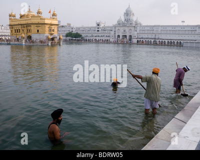 Sikhs clean the Sarovar (water tank) – around the Golden Temple (Sri Harmandir Sahib); others bathe. Amritsar. Punjab. India. Stock Photo