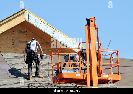 Construction workers laying shingles on roof exterior of new building Stock Photo