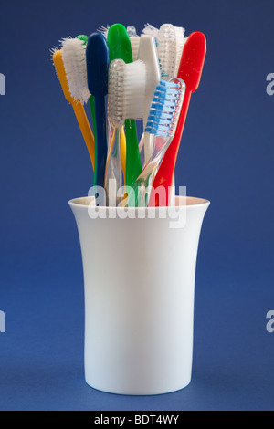 Old toothbrushes of varied colors in a white ceramic round container with a blue background Stock Photo