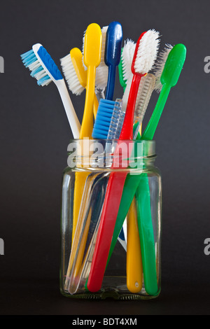 Old toothbrushes of varied colors in a square glass jam jar with a black background Stock Photo