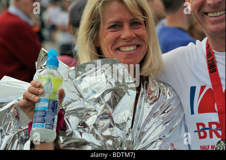 Young woman runner in foil wrap holding drink after Bristol Half Marathon, UK Stock Photo