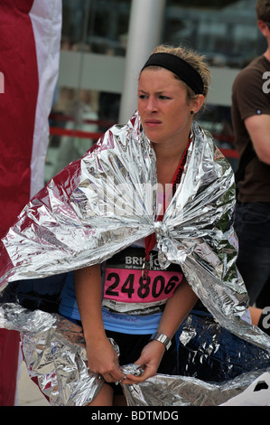 Young woman runner in foil wrap recovering and watching other runners after Bristol Half Marathon, UK Stock Photo