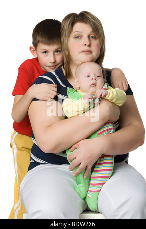 Mother sits on achair and holds infant on hands, elder son embraces her for shoulders, isolated on white Stock Photo