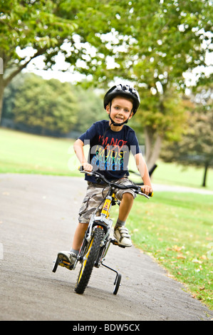 Vertical close up portrait of a young boy riding his new bike with stabilisers in the park Stock Photo