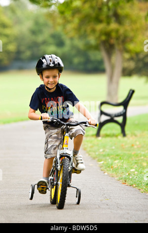 Vertical close up portrait of a young boy riding his new bike with stabilisers in the park Stock Photo