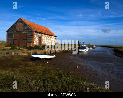 Small boats moored in the old harbour at Thornham North Norfolk with an isolated building a former coal store Stock Photo