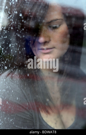 portrait of a dark haired woman with eyes closed through a rain soaked window Stock Photo