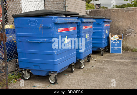 Three large blue plastic commercial wheelie bins full of rubbish / garbage in enclosed yard Stock Photo