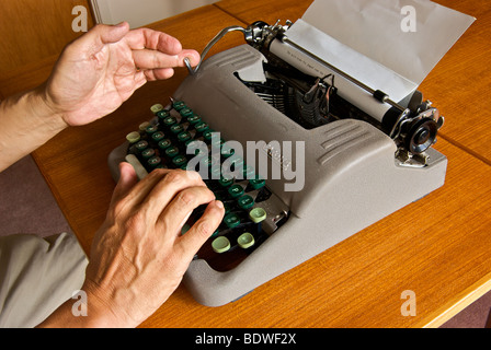 Outdated technology manual portable typewriter finger pushing on carriage return to advance paper on drum roller Stock Photo