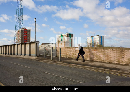 A man in a suit carrying a bag walks to work past high rise block of flats in Hull city center. Stock Photo