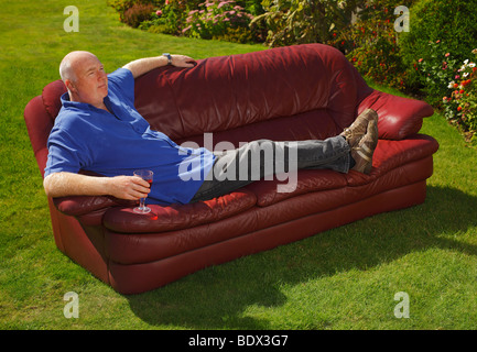 Man sitting in the garden on a sofa, with a glass of wine. Stock Photo
