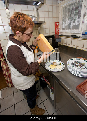 Chef in fondue restaurant in Swiss village of Leukerbad prepares raclette, an alpine cheese dish Stock Photo