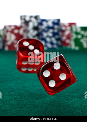 Two red dices rolling over a green felt. Out of focus stack of colorful chips on the background. Stock Photo