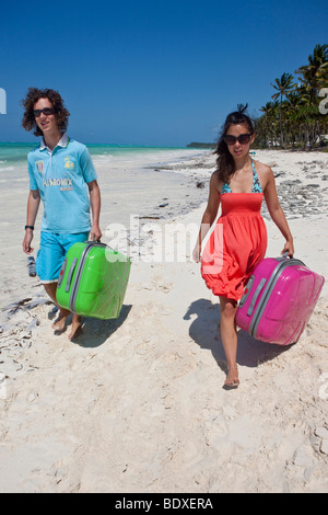 Two teenagers on holiday carry their suitcases at the beach Stock Photo