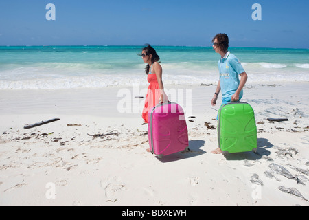 Two teenagers on holiday carry their suitcases at the beach Stock Photo