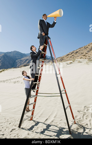 Business People on Stepladder Using Megaphone in Desert Stock Photo