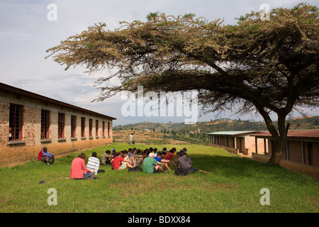 A group of English public schoolboys and staff sit and reflect under the shade of a tree at the Murambi Genocide Memorial Museum Stock Photo