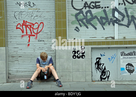 Lonely nine-year-old boy in front of a closed shop smeared with graffiti, Germany, Europe Stock Photo