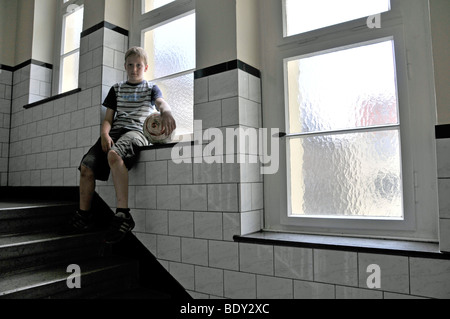 Lonely nine-year-old boy with football in the hallway, Germany, Europe Stock Photo