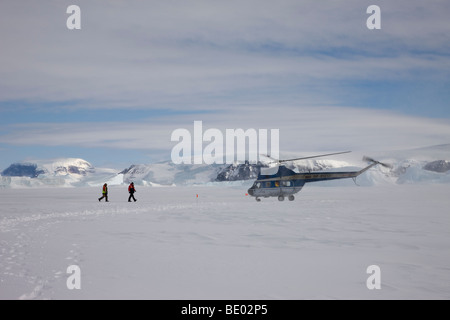 2 men approach landing Helicopter on snow covered mountainous Snow Hill Island in Antarctica Stock Photo